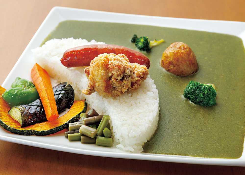 緑色のカレールーに唐揚げ、ウインナー、素揚げ野菜などがトッピングされている。
